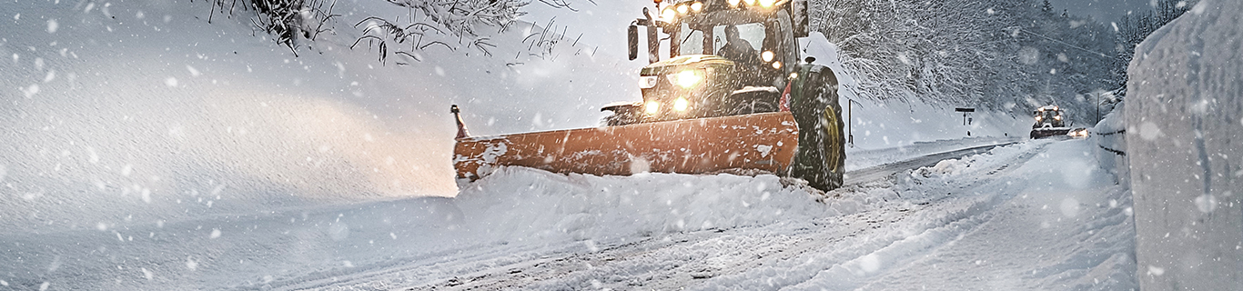 Snow plow clearing a snowy road at night during a state of emergency winter storm